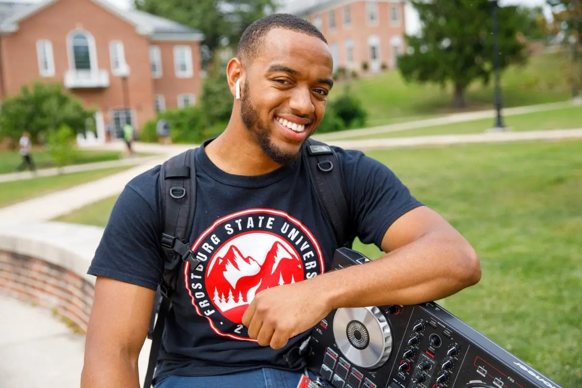 student smiling while outside and holding a boom box