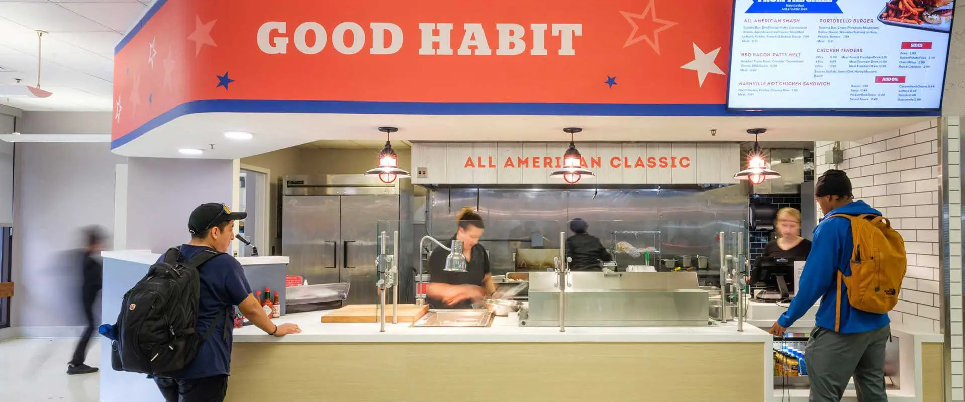 The image shows two customers standing at a food counter labeled "GOOD HABIT" inside a bright, clean dining area, with workers behind the counter preparing and serving food.
