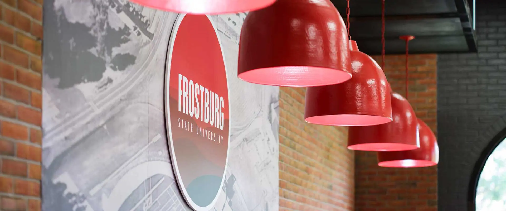 a row of red pendant lamps hanging from the ceiling inside a modern indoor space with exposed brick walls and a large wall sign that reads "FROSTBURG."